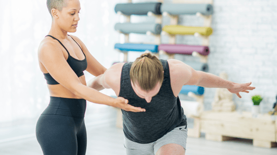 Female yoga therapist of colour providing yoga therapy to a young white male yoga student